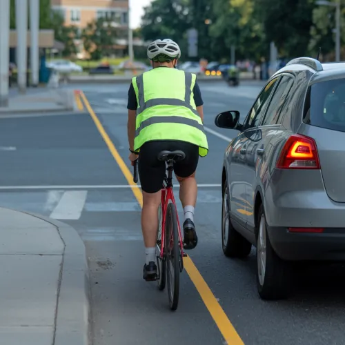 A cyclist with a helmet and reflective vest is riding near a car at an intersection, symbolizing the type of right hook accidents that occur in a bicycle lane.