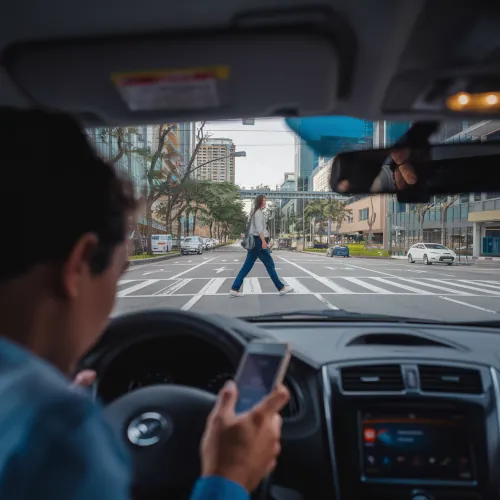 A driver looking at their phone while a pedestrian is crossing the street, illustrating how distracted driving can lead to pedestrian accidents.